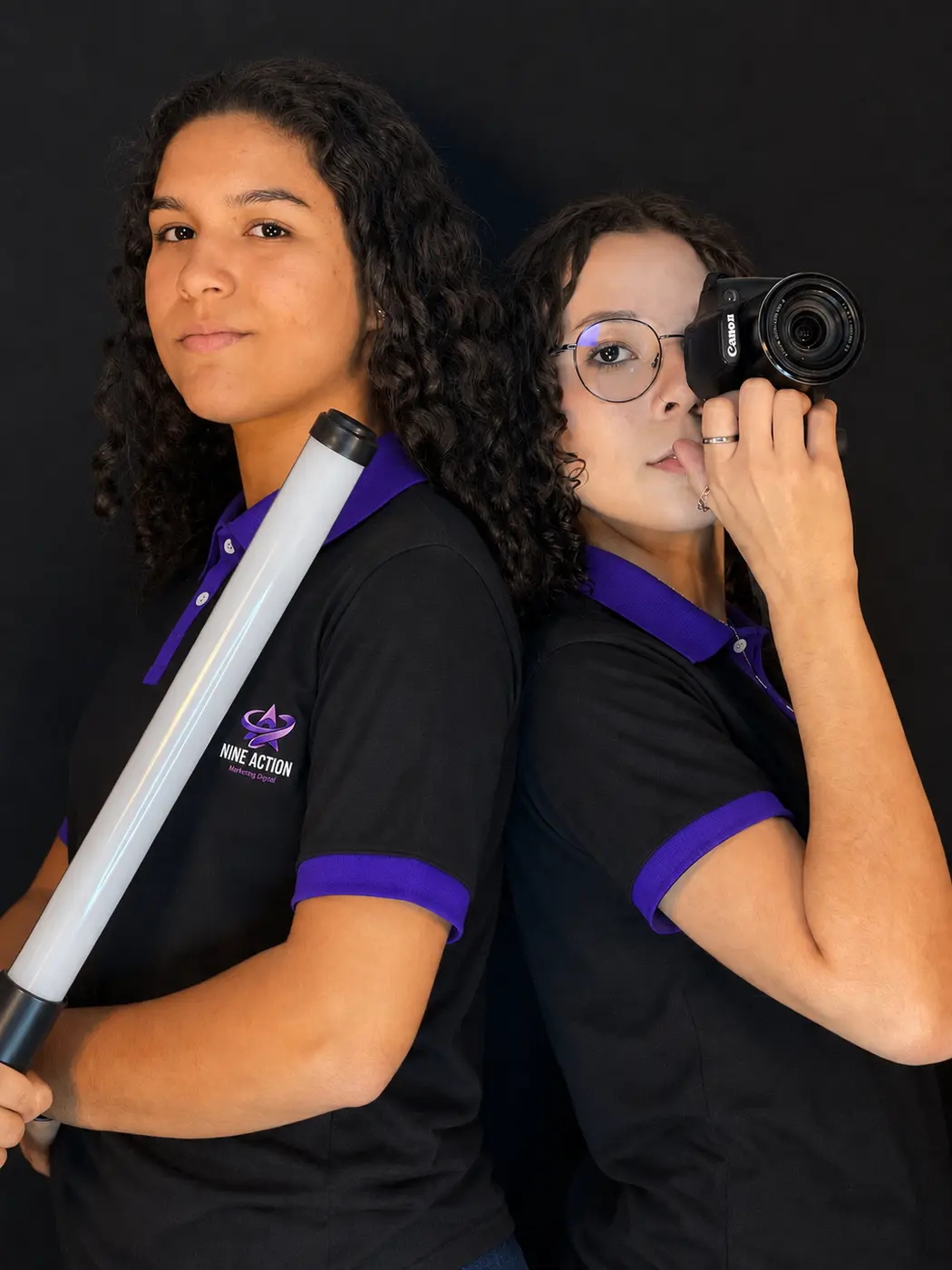As duas sócias da Nine Action de costas uma para a outra: uma segura um bastão de luz, a outra uma câmera fotográfica